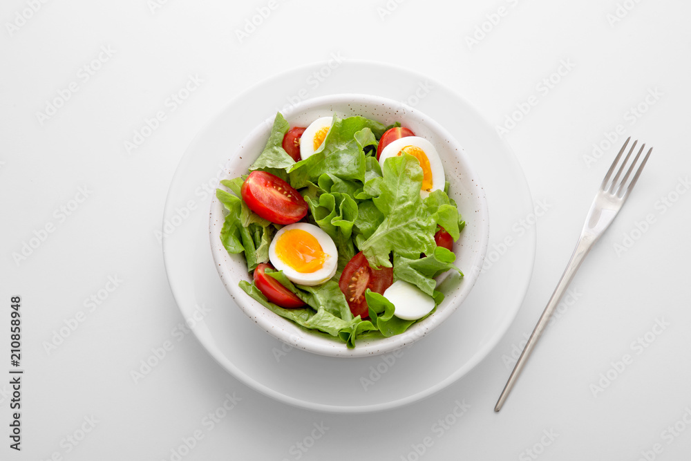 Fresh salad meal with letuce, eggs and tomato in a white bowl with a fork on the side viewed directly from above. Fresh organic vegetable snack viewed from above. Top view. Copy space Fresh salad meal with letuce, eggs and tomato in a white bowl with a fork on the side viewed directly from above. Fresh organic vegetable snack viewed from above. Top view. Copy space