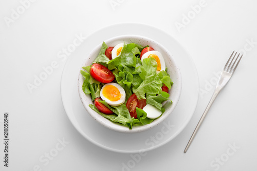 Fresh salad meal with letuce  eggs and tomato in a white bowl with a fork on the side viewed directly from above. Fresh organic vegetable snack viewed from above. Top view. Copy space