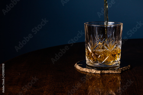 Whiskey being poured into a crystal tumbler on a dark wooden table