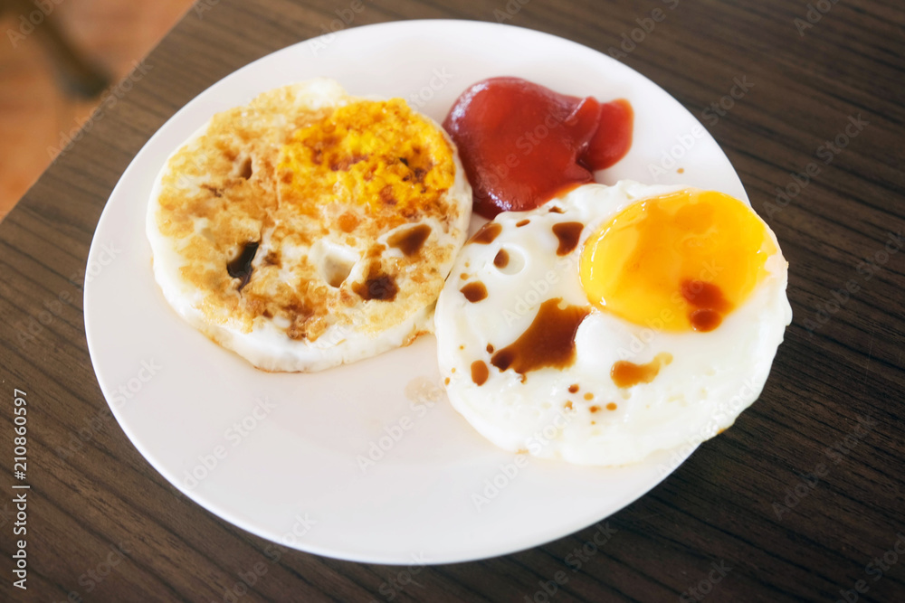 Two fried eggs with tomato sauce and soy sauce in white plate on wooden table for breakfast.. Two fried eggs with tomato sauce and soy sauce in white plate on wooden table for breakfast..
