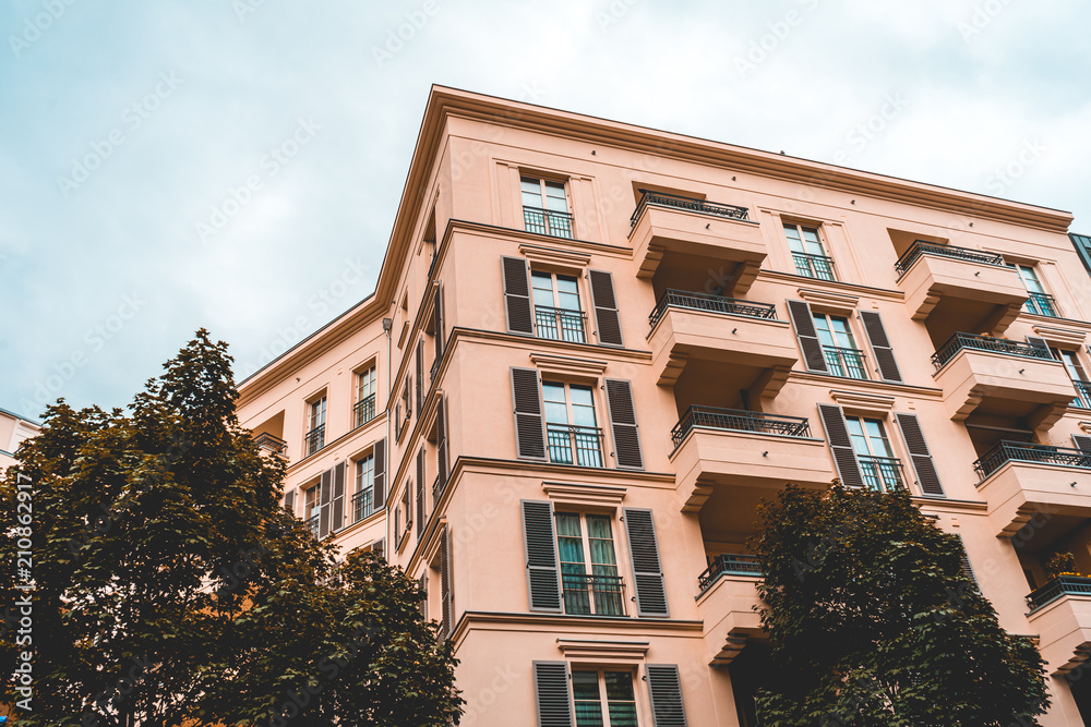 Fototapeta premium orange apartment building with green trees and cloudy sky