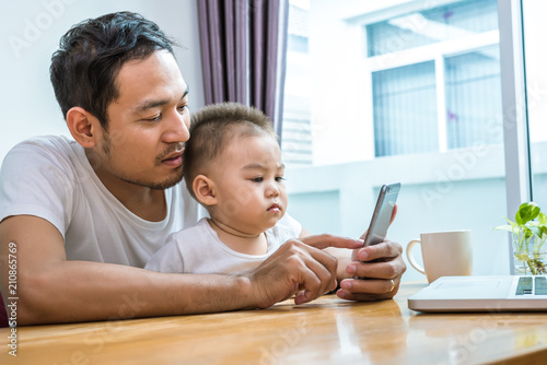 Asian father and son using smart phone together in home background. Technology and People concept. Lifestyles and Happy family theme. Internet and communication theme photo