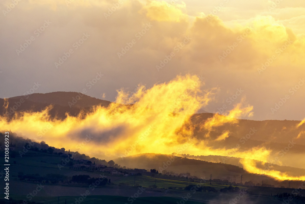 Obraz premium Low clouds over a rolling landscape at sunset