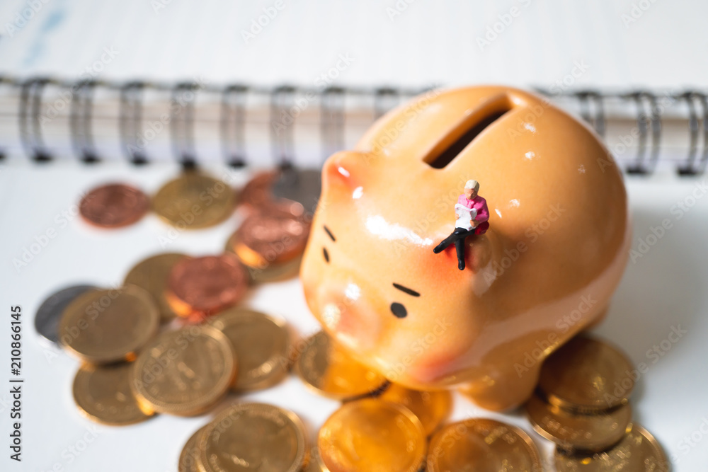 Miniature people, woman reading on piggy bank and stack coins background using as business and financial concept Miniature people, woman reading on piggy bank and stack coins background using as business and financial concept