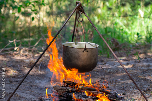 Tourist pot hanging over the fire on a tripod. Cooking in the campaign