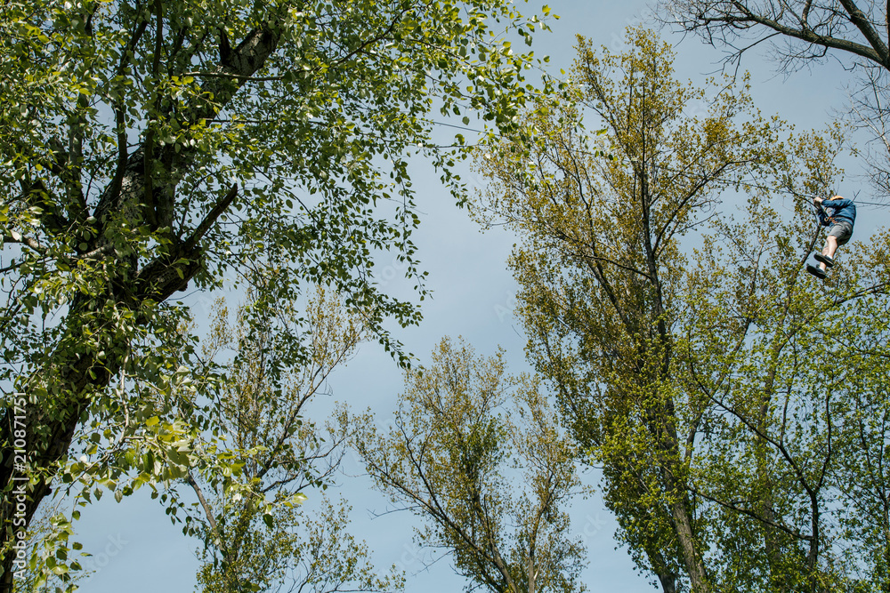 Tourism. Active rest in parks and forests. Cableway between the trees. A man sits on a rope from a tree. Mountaineering. Tourism. Active rest in parks and forests. Cableway between the trees. A man sits on a rope from a tree. Mountaineering.