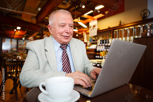 business, technology and people concept - old senior businessman in suit and tie with laptop computer drinking coffee in city cafe