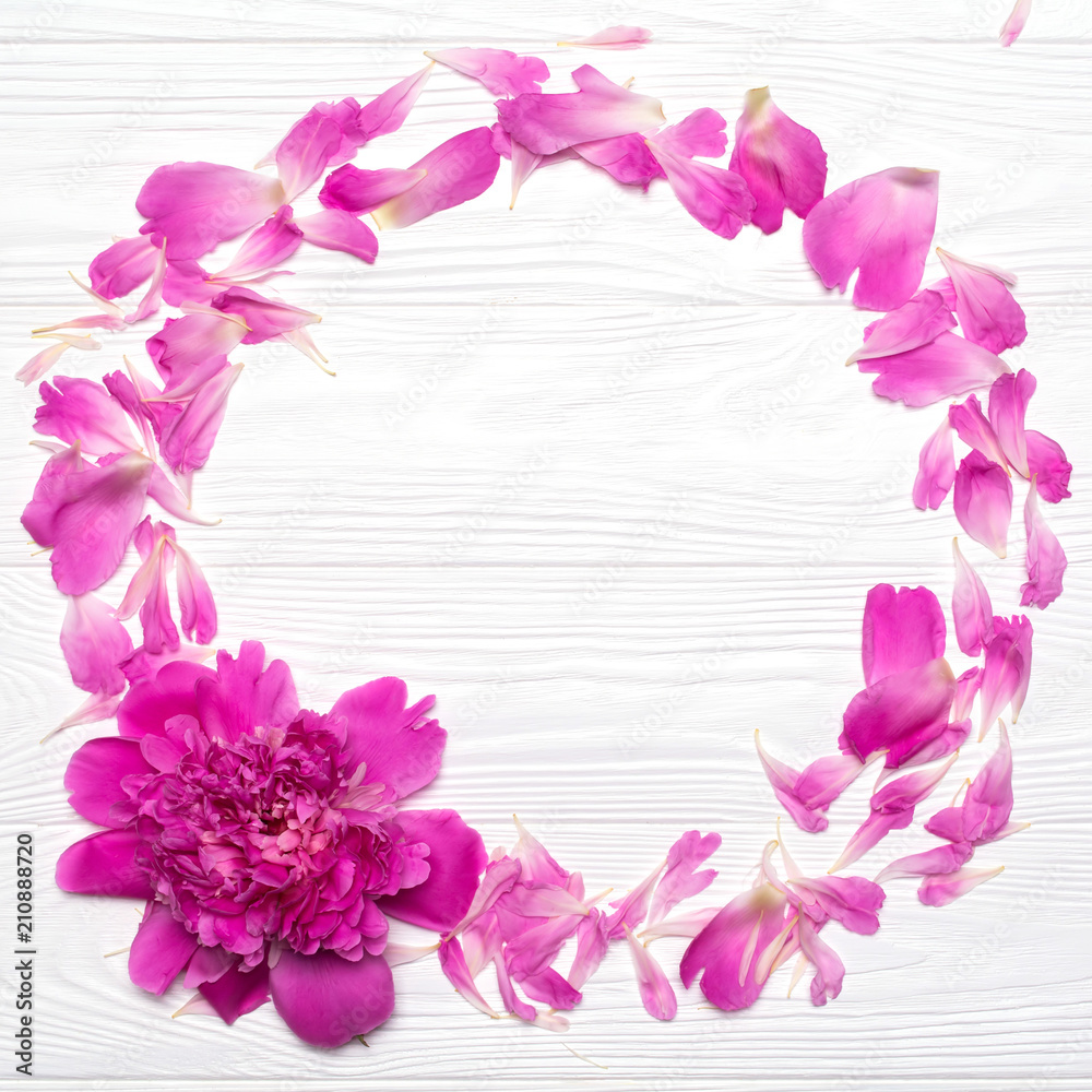 Round frame of petals and peony flower on a white wooden background.