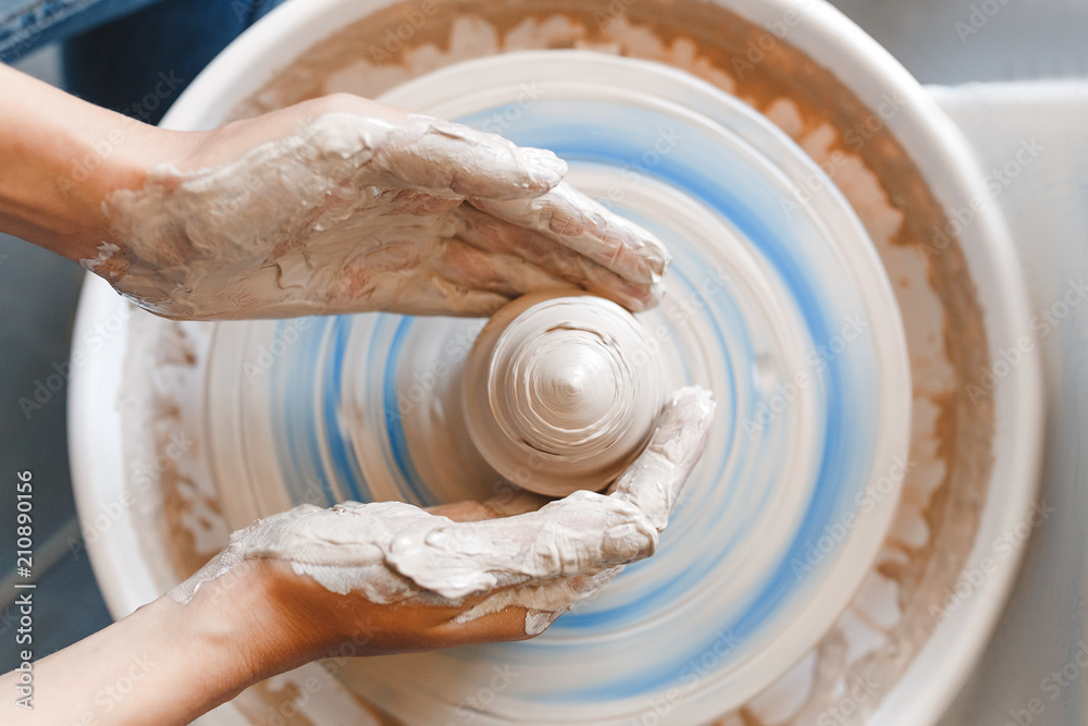 Top view of hands with clay making of a ceramic pot on the pottery wheel, hobby and leisure with pleasure concept - obrazy, fototapety, plakaty 