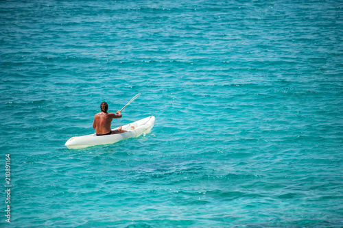 A man on a vacation day relaxed with the kayak  in a bay on the turquoise and crystalline Mediterranean sea in Sardinia.