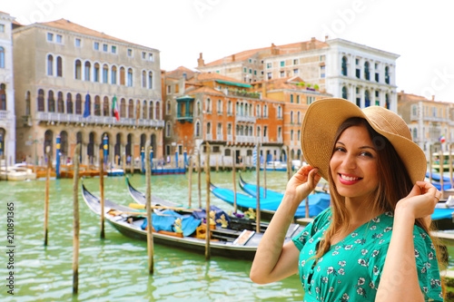Holidays in Venice! Beautiful woman with straw hat smiling at camera with Venice Grand Canal, gondolas and palaces on the background.