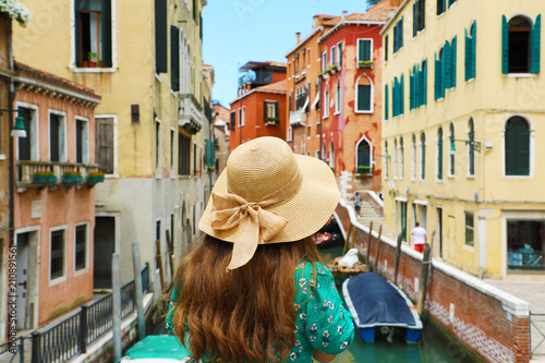 Back view of young woman with straw hat looking at Venice colorful buildings from a bridge on canal, Venice, Italy