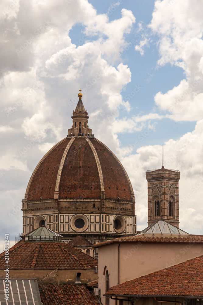 The Duomo cathedral and Campanile in Florence amidst a cloud-filled blue sky.