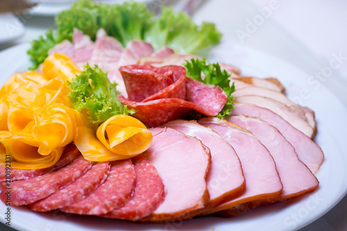 Fine meat dish with leaf lettuce on a festive table. Sliced sausage and meat on a plate_