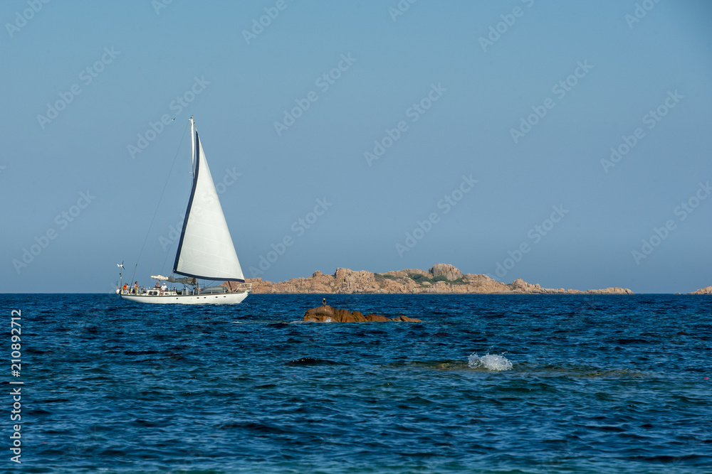 On a sunny summer day a white sailboat sails on Mediterranean Sea in Sardinia, luxury vacations.