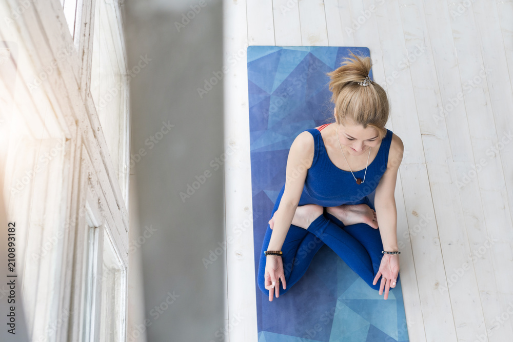 Top view of beautiful young fitness woman in blue jumpsuit working out on white wooden floor at home, doing yoga exercise, full length