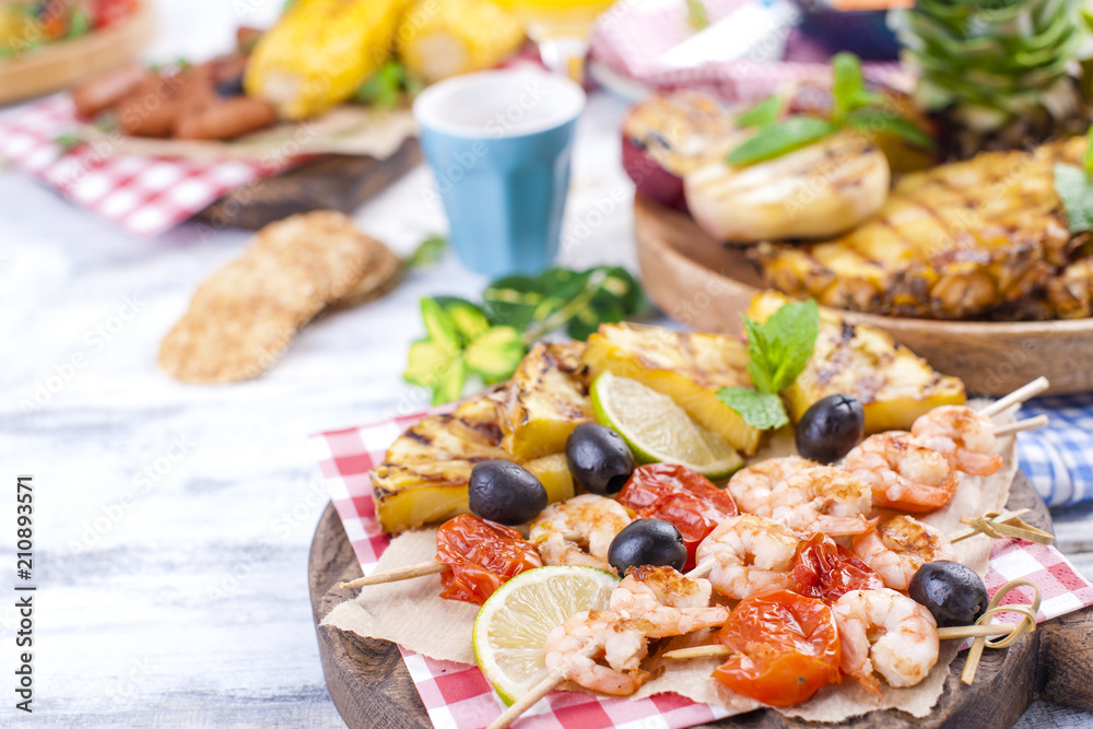 Fototapeta premium Vegetables, fruits and shrimp on the grill, for a summer lunch. Healthy food. Appetizers on a white background. Copy space.