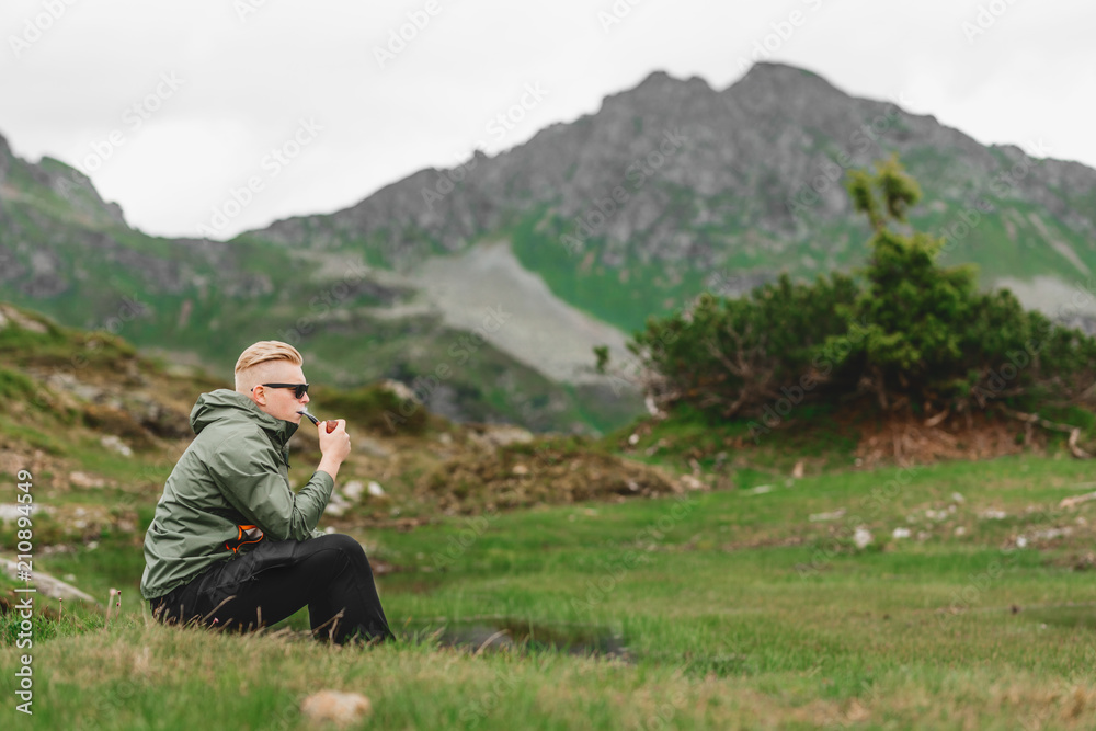 Mann wandert durch die Berge, sitzt und raucht Pfeife Mann wandert durch die Berge, sitzt und raucht Pfeife