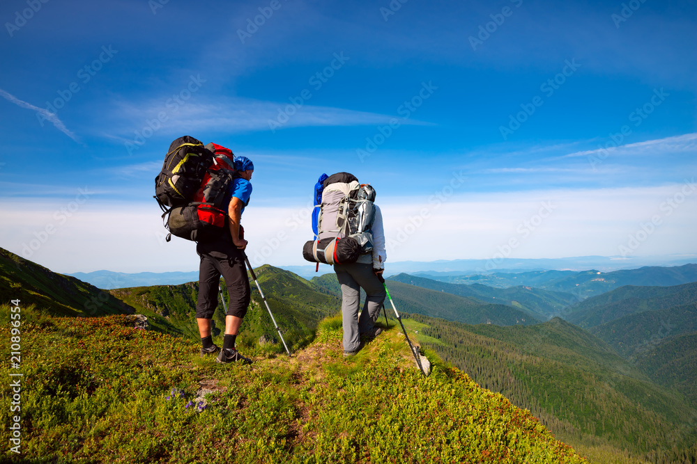 Adventurers with backpacks stands on green mountain ridge