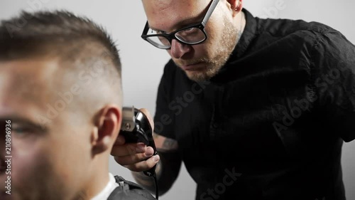 Tattoed barber makes haircut for customer at the barber shop by using hairclipper, man's haircut and shaving at the hairdresser, barber shop photo