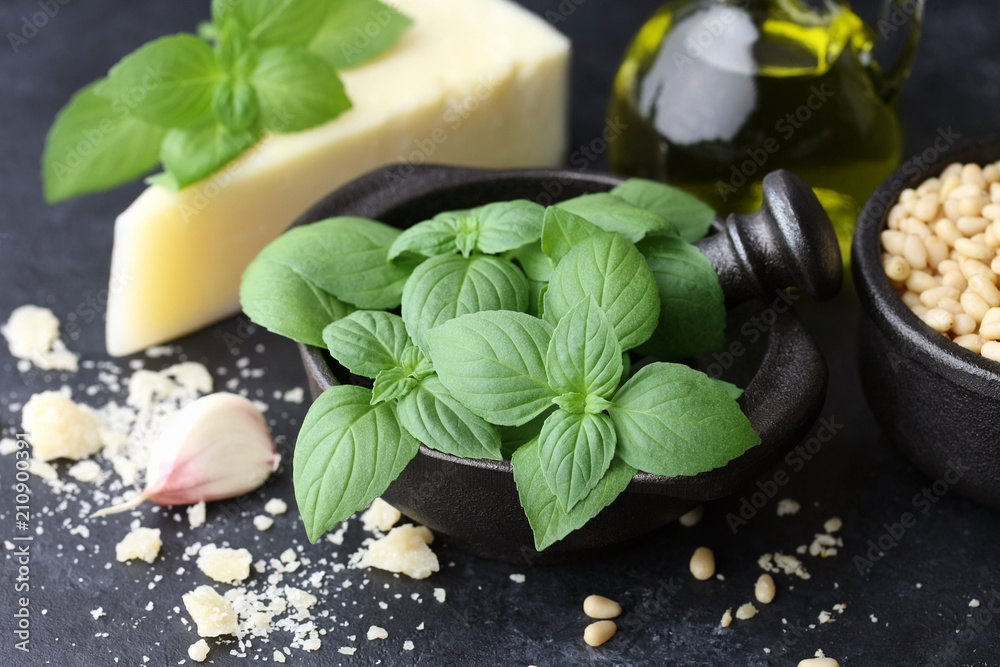 Basil leaves, parmesan cheese and other pesto sauce ingredients on black stone background