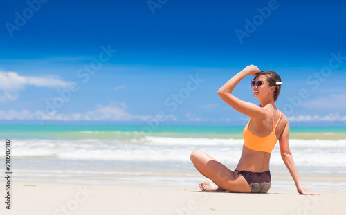 young longhaired woman in sunglasses and bikini smiling and sunbathing by the beach