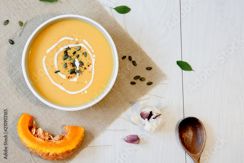 Pumpkin soup with pumpkin seeds. In white bowl, on hessian fabric. With rustic spoon and garlic. 