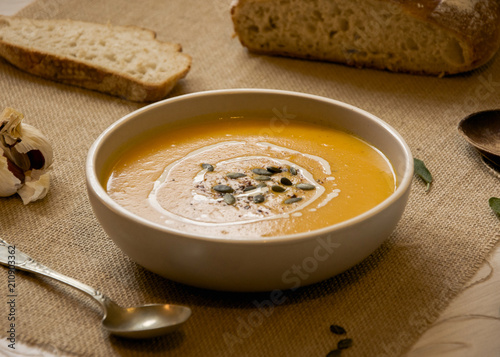 Pumpkin soup with pumpkin seeds. In white bowl, on hessian fabric. With silver spoon and wholegrain rustic bread. 