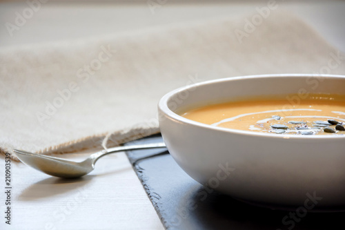 Pumpkin soup with pumpkin seeds. In white bowl, on a slate board with sliver spoon and hessian fabric. 