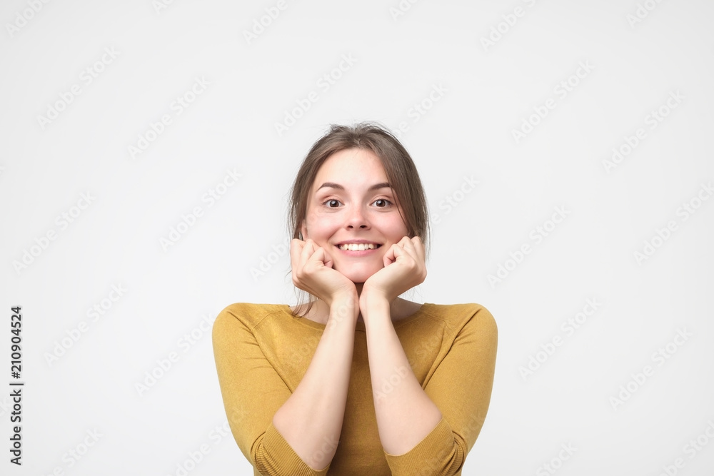 Close up portrait of young happy caucasian woman in yellow sweater on white background. She is holding arms near face. Concept of positive facial emotion. Close up portrait of young happy caucasian woman in yellow sweater on white background. She is holding arms near face. Concept of positive facial emotion.