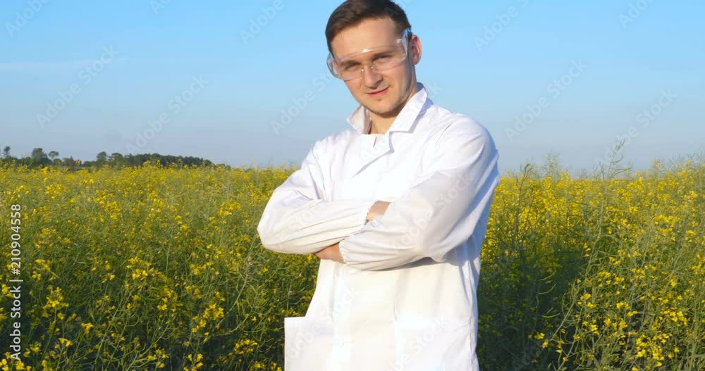 Portrait of a young handsome biologist or agronomist in white medical clothes, safety glasses, smiling, successful, field of canola, bio. Portrait of a young handsome biologist or agronomist in white medical clothes, safety glasses, smiling, successful, field of canola, bio.