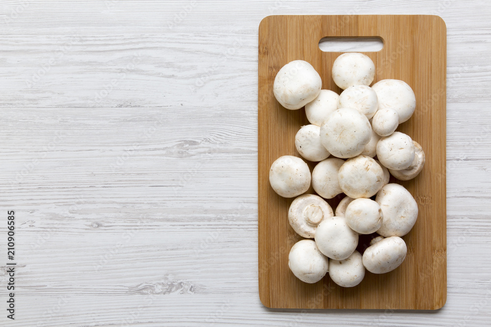 Champignon mushrooms on bamboo board on a white wooden table, top view. From above. Copy space. Champignon mushrooms on bamboo board on a white wooden table, top view. From above. Copy space.