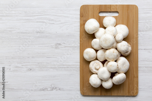 Champignon mushrooms on bamboo board on a white wooden table, top view. From above. Copy space.