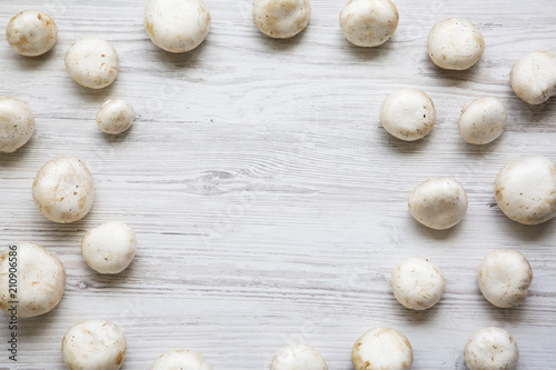 Champignon mushrooms on a white wooden background, top view. From above. Copy space.