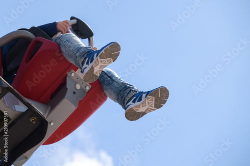 children's legs hang from a carousel seat high up against the blue sky, carnival fun at the fairground with copy space