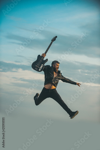 Freedom in his veins. Freedom, bearded man jump with guitar on blue sky