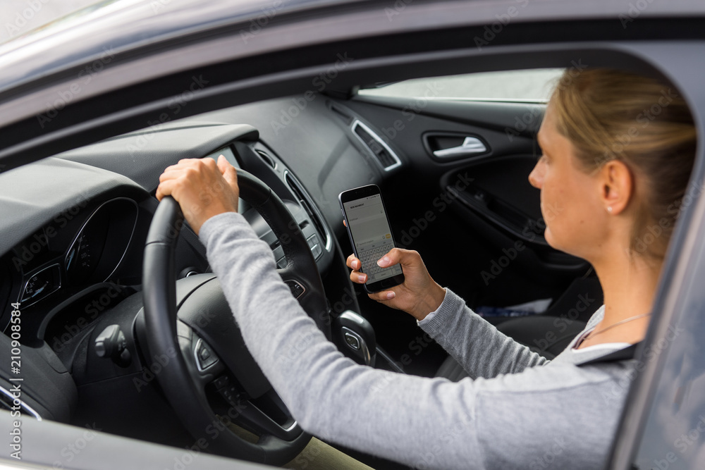 Junge Frau tippt SMS beim Autofahren