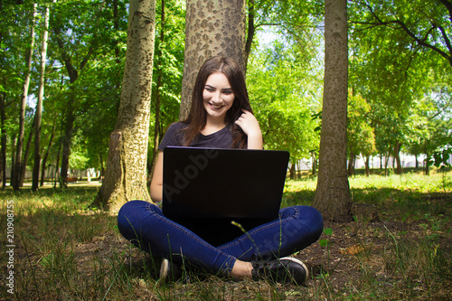 girl with a laptop sitting near a tree.