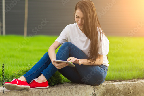 young brunette womanwith tablet serfing in internet on grass