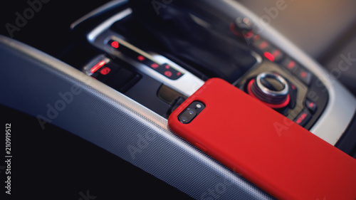 smartphone in red case with dual camera in the interior of a modern luxury car