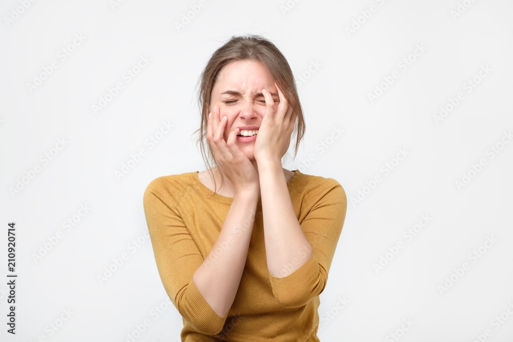 Exhausted young woman in yellow sweater touching her head with eyes closed. Female exchange worker suffering from insomnia. She is overworked. Preparing for difficult exam Exhausted young woman in yellow sweater touching her head with eyes closed. Female exchange worker suffering from insomnia. She is overworked. Preparing for difficult exam