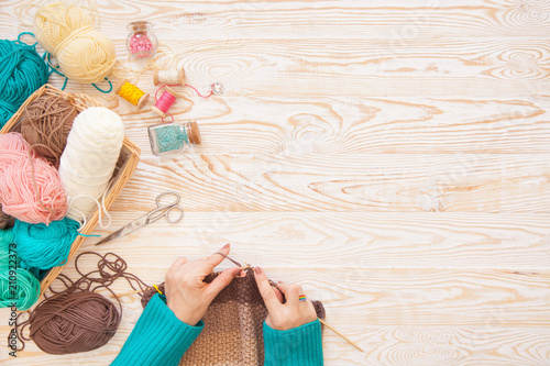 A woman knits a white and broun knitted fabric of woolen yarn. Knitting needles. Aged background. Turquoise and white.