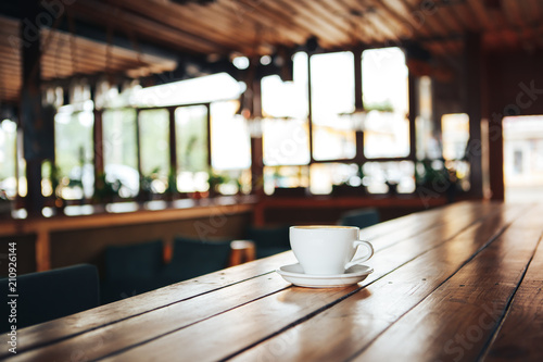 Hot coffee in white cup on wooden table. White cup of coffee on a wooden table in a cafe. Good morning with a ceramic white cup of coffee in a cafe 