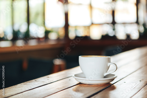 Hot coffee in white cup on wooden table. White cup of coffee on a wooden table in a cafe. Good morning with a ceramic white cup of coffee in a cafe 