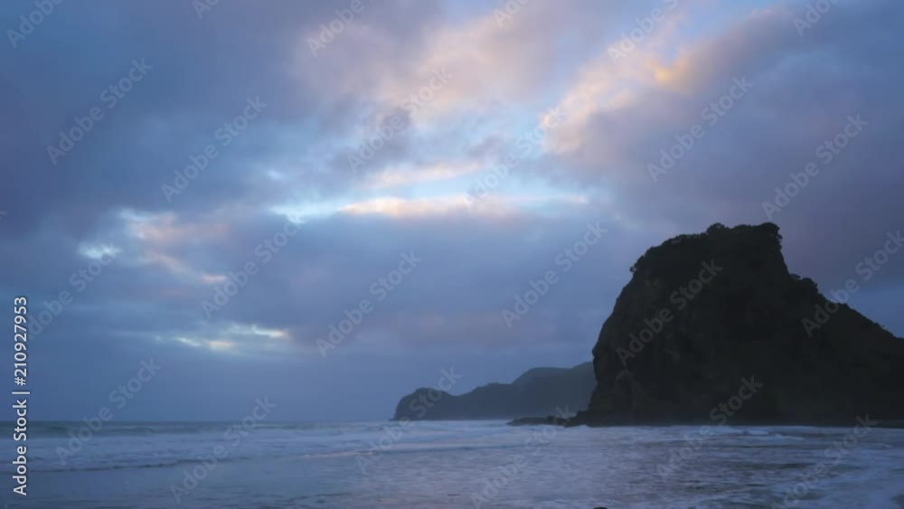 Gentle waves on beach at dusk under heavenly light purple pink sky with rocky distant coastline Gentle waves on beach at dusk under heavenly light purple pink sky with rocky distant coastline