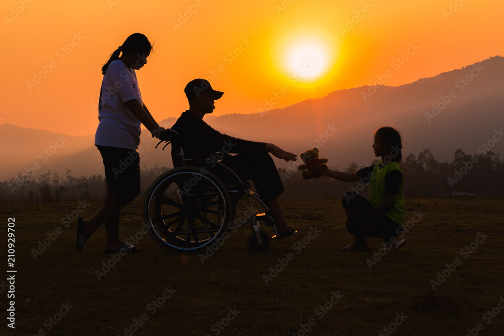silhouetts disabled man is sitting on wheelchairs at sunset time with children helping he.