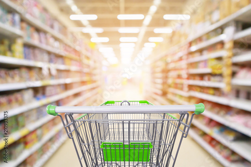 Supermarket aisle product shelves interior blur background with empty shopping cart