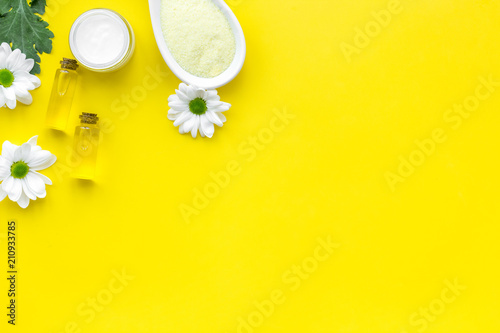 Natural organic spa cosmetics for skin care with chamomile. Spa salt, cream, oil on yellow background top view copy space