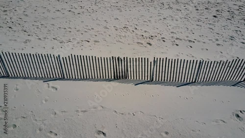 Low Aerial: Footsteps recorded in the sand near a wooden fence on the beach