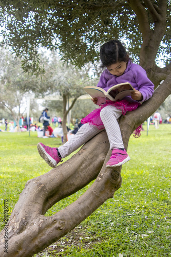 Cute little girl reading a book on a tree